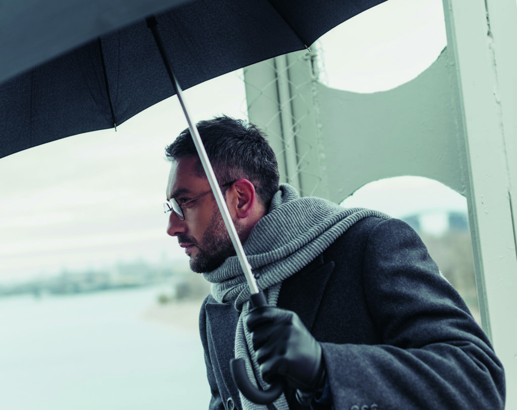 stilvolle erwachsenen Mannes in Schal und Mantel mit Regenschirm auf Brücke